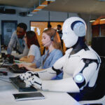 Robot working at computer among people. Maschine typing on keyboard in office. IT team of future. Futuristic worker. Humanoid work at call center. Support job. Selling concept. Technologies.